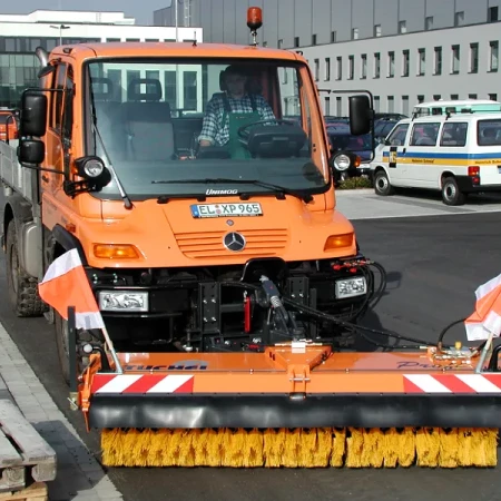 Véhicule balayeuse de rue orange, équipé pour nettoyer les voies urbaines
