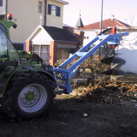 Tracteur vert équipé d'une tarière pour percer des trous, utilisé sur un chantier
